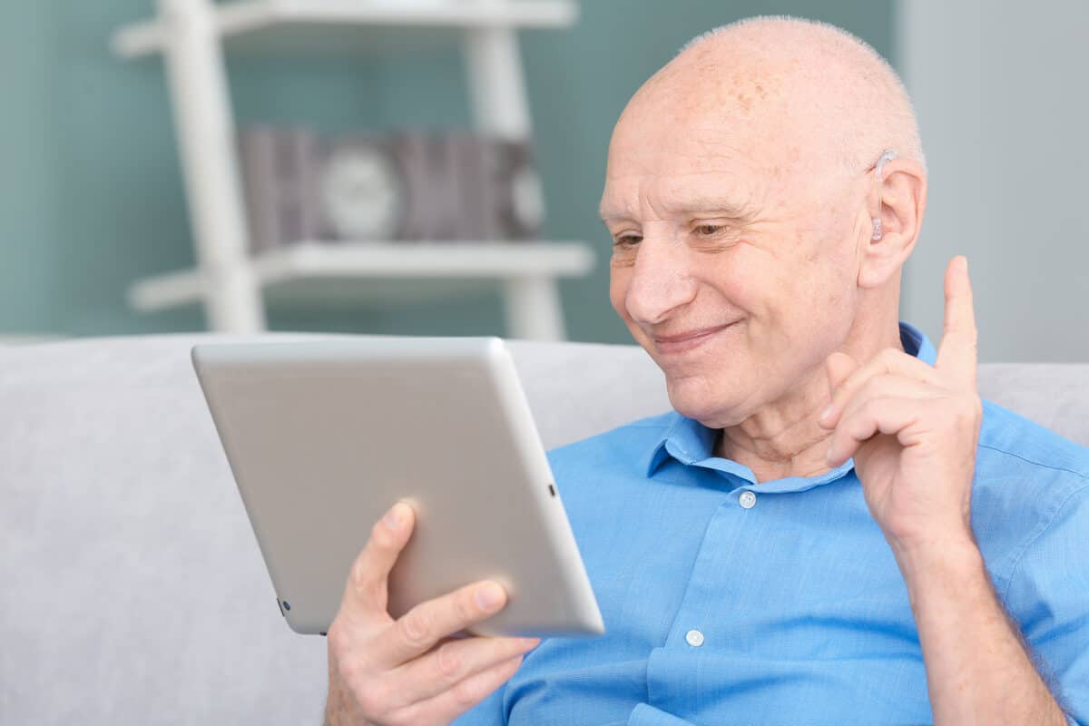 Senior man with hearing aid using tablet computer indoors